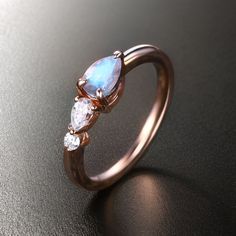 a rose gold ring with three pear shaped blue opal and diamond accents, on a black surface