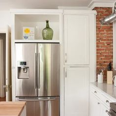 a stainless steel refrigerator in a kitchen with brick wall and white cabinetry, along with an island