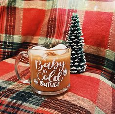 there is a glass mug with some liquid in it on the plaid blanket next to a small christmas tree