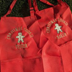 two red aprons with embroidered gingerbread cookies on them sitting in the grass next to each other