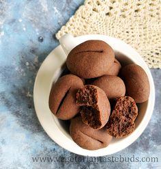 a white bowl filled with chocolate cookies on top of a blue tablecloth next to a crocheted doily