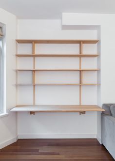 an empty white room with wooden shelves on the wall and a gray couch in front of it