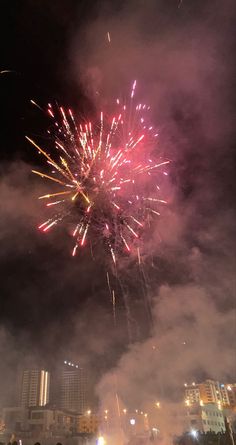 fireworks are lit up in the night sky with buildings and lights behind them as people watch