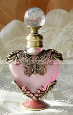 a pink heart shaped bottle sitting on top of a white lace covered tablecloth next to a glass ball