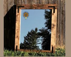 a mirror sitting in the grass next to a wooden fence with trees reflected in it