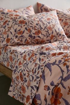 an orange and purple flowered comforter on a bed with matching pillowcases