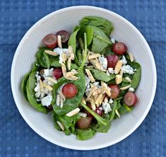 a white bowl filled with spinach, grapes and feta cheese on top of a blue table cloth