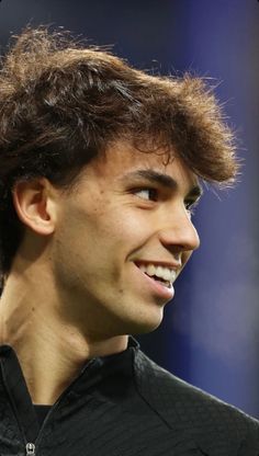 a close up of a person wearing a black shirt and looking to the side with a smile on his face