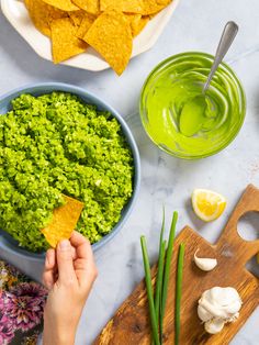 someone dipping guacamole into a bowl with tortilla chips on the side