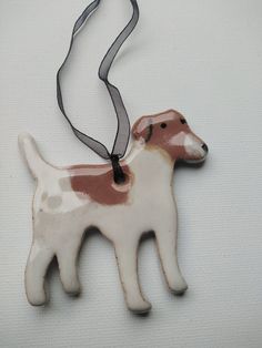 a white and brown dog ornament hanging from a black ribbon on a white background