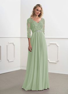 a woman in a long green dress standing next to a white wall and posing for the camera