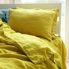 a bed with yellow sheets and pillows in front of a window