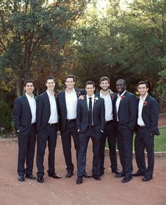 a group of young men standing next to each other in front of trees and bushes