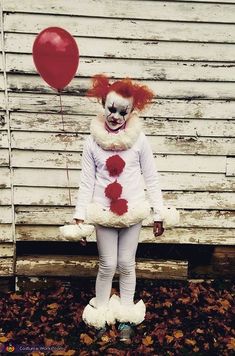 a child dressed as a clown holding a red balloon