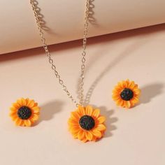 three sunflower necklaces and earrings on a white surface