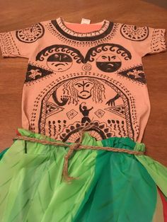 a child's t - shirt and green skirt on a wooden table with a string