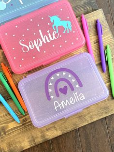 three personalized lunch boxes with pencils and markers next to them on a wooden surface