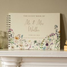 a wedding guest book sitting on top of a white mantle next to a vase with flowers