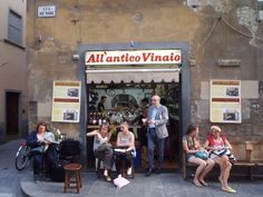 several people sitting on benches in front of a store with an open door that says, all'antio vinato