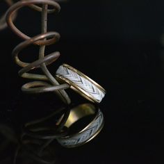 two gold rings sitting on top of a black surface next to a metal object with an intricate design