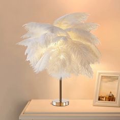 a white lamp sitting on top of a table next to a framed photo and a painting