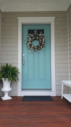 a blue front door with a wreath and potted plant on the porch next to it