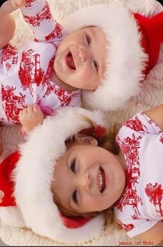 two young children laying on top of a blanket wearing christmas pajamas and santa claus hats