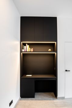 an empty room with a desk and bookshelf next to the door, in front of a white wall