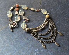 I love how soft and pretty this necklace is. Yellow quartz pairs beautifully with the faceted crazy lace agate and peach moonstone. Lots of silver accent beads and additional swarovski crystals adds a touch of sparkle. Layers of czech glass beads, leaf charms, and antique silver chains drape from a curved tube bead giving it lots of movement and interest. Finished off with a leaf patterned silver plated toggle clasp. Length: 10 3/4"All components and materials used in this design are listed in t Luxury Artisan Soldered Necklaces, Bohemian Apricot Jewelry For Gift, Handmade Bohemian Apricot Jewelry, Handmade Apricot Bohemian Jewelry, Boho Statement Necklace, Tube Necklace, Multi Chain Necklace, Modern Necklace, Yellow Quartz