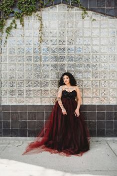 a woman standing in front of a wall wearing a black and red dress with her hands on her hips