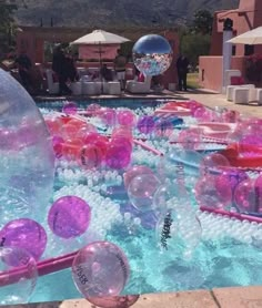 a pool filled with lots of bubbles and pink balls in the water next to some buildings