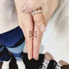 a woman's hand with a small bow tattoo on the middle finger and two fingers