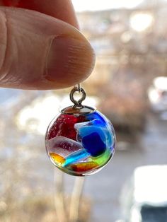 a hand holding a small glass ball with colorful liquid in it's center on a chain