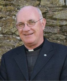 an older man wearing glasses standing in front of a stone wall