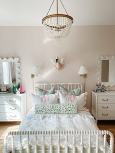 a white bed sitting under a chandelier next to a dresser with drawers and lamps