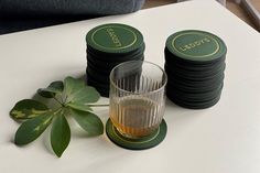 a stack of black and green coasters next to a glass on a white table