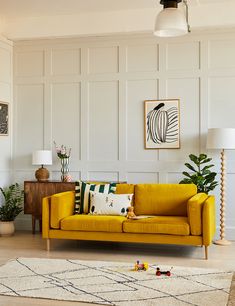 a living room with a yellow couch, rug and potted plants on the floor