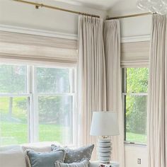 a living room filled with lots of furniture next to two windows covered in white drapes