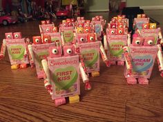 small pink boxes with eyes and noses on them sitting on a wooden table in front of toy cars