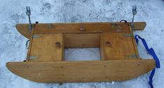 a wooden boat sitting on top of snow next to a blue ribbon and some metal handles