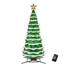 a green and white christmas tree with lights next to a remote control on a stand