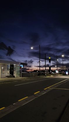 an empty street at night with the sun setting in the distance and some lights on