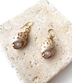 Handmade from natural shells and gold-plated sterling silver, these earrings are designed with little secret inside - freshwater pearls. They coordinate effortlessly with beachwear and bright color summer dresses. Product details: Composition: shells, pearls, gold plated silver Measures 4.5 cm Handmade in Spain Free shipment worldwide Summer Pearl Earrings For Pierced Ears, Summer Pearl Earrings, Gold Drop Earrings For Vacation, Elegant Pearl Charm Shell For Beach, Elegant Shell-shaped Earrings For Vacation, Yellow Gold Shell Jewelry For Beach, Summer Beach Jewelry With Mother Of Pearl, Elegant Beach Shell With Pearl Charm, Beach Pearl Charm Shell Earrings