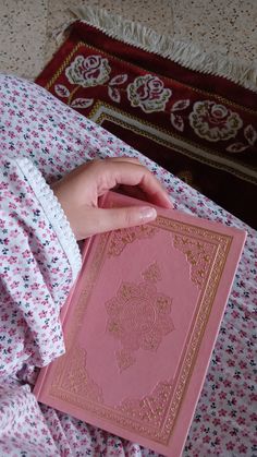 a person holding a pink book in their hand on top of a floral print bed spread