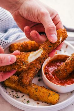 two hands reaching for some fried food on a plate with dipping sauce in the bowl