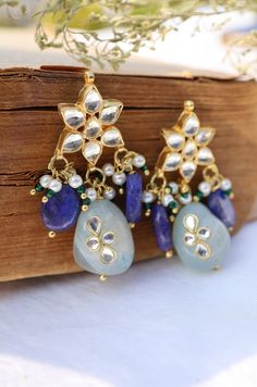 The Nessa kundan studs features beautiful myriad of kundan and blue stone drops. The versatile pair is replete with style and glamour. Closure - Push Back. There's a subtle yet clearly indisputable quality in our traditional attires that brings out the depth of a woman's femininity. The warm glory of the gold, the ritualistic richness of red and green, the clamor of payals and kadas, are a celebration of womanhood. The magic is in the gaze of the woman, her suave as she walks, shy of her own glo Blue Danglers For Diwali Gift, Blue Danglers For Diwali Celebration, Blue Temple Jewelry Earrings For Festive Occasions, Blue Kundan Danglers For Gift, Blue Kundan Danglers As A Gift, Blue Fusion Earrings With Latkans, Blue Temple Jewelry Earrings With Latkans, Blue Latkans Earrings For Celebration, Traditional Blue Kundan Earrings