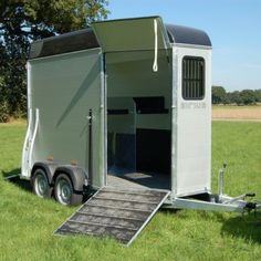 a horse trailer with the door open on a green grass covered field next to trees