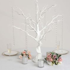 a white tree with flowers and candles on a table next to two plates that have silverware in them