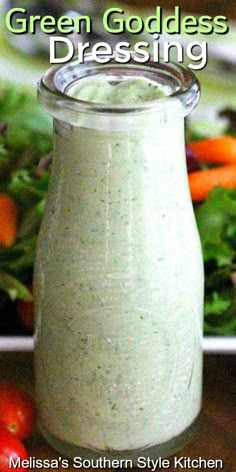 green goddess dressing in a glass jar on a wooden table with salad and vegetables behind it