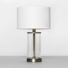 a glass table lamp with a white shade on the base and a gold metal frame